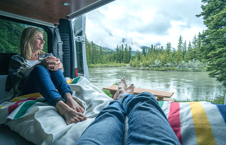 A girl looks out from a camper van at the lake