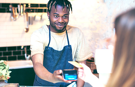 A male barista holds a payment terminal for a customer to tap