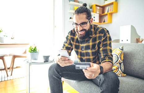 A man sitting on a couch while buying something on his phone