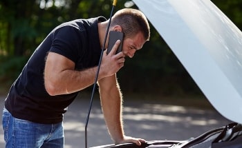 A man talking on a cellphone while looking into the front engine of a car