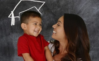 A smiling mother holding up her son to a chalkboard with a graduation cap drawn on it