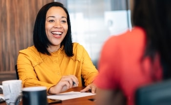 A smiling woman looking at another person from across a table