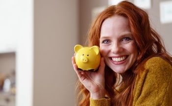 A smiling young women holding up a yellow piggy bank