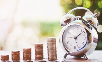 Coins increasingly stacked to look like a graph next to an old alarm clock