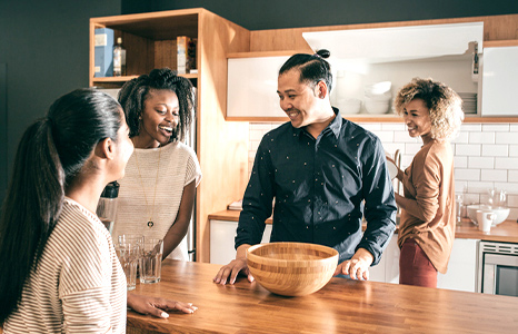 Four friends gather around a kitchen counter and  socialize