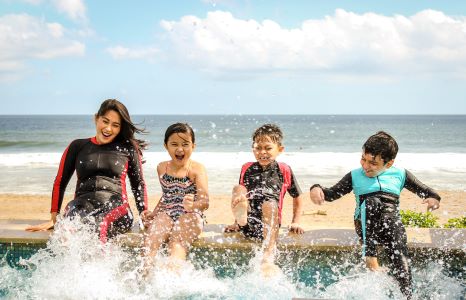 Three kids and a young women in wet suits splashing their feet in a pool